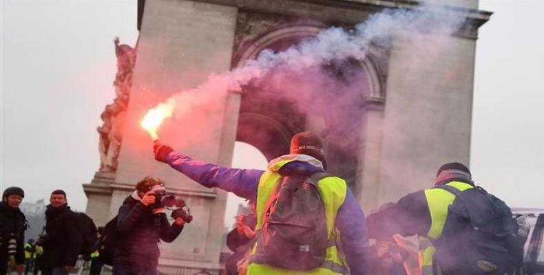 A demonstrator brandishes a flare with the Arc de Triomphe in background during a protest of Yellow Vests (Gilets jaunes) against rising oil prices and living c