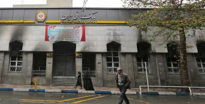 Iranians walk past the branch of a local bank damaged during demonstrations in Tehran.  (Photo: AFP)