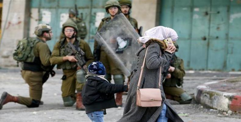 A woman and a child walk past Israeli troops during clashes with Palestinian demonstrators at a protest in Hebron.   (Photo by AFP)