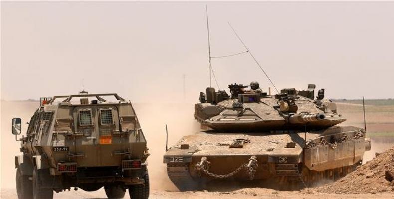 An Israeli army armored vehicle driving past a Merkava Mark IV tank taking position along the Gaza fence.  Photo: AFP