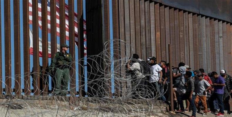 Central American migrants look through a border fence as a US Border Patrol agent stands guard near the El Chaparral border crossing in Tijuana, Mexico, on Nove