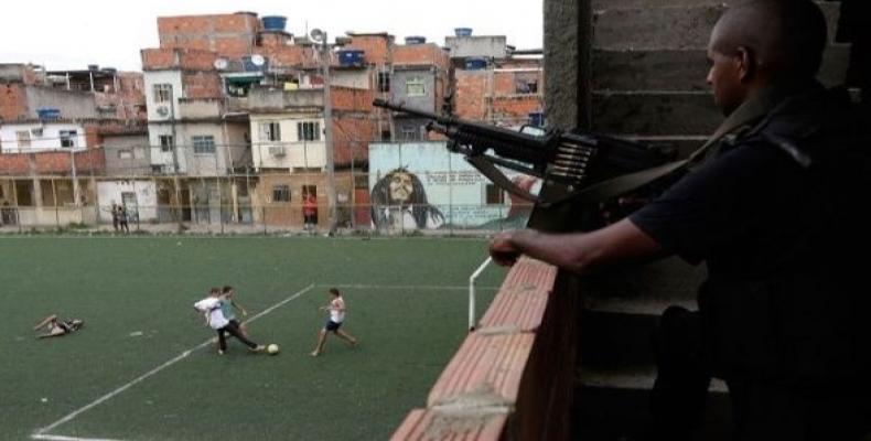 Boys play football as an armed soldier looks on in Mare Favela Complex in Rio de Janeiro, Brazil.  Photo: Reuters