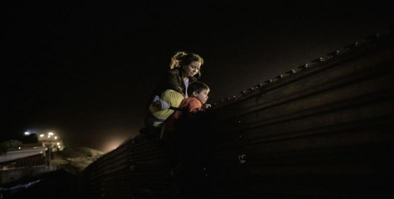A migrant family from Honduras climbs the border fence Wednesday, hoping to enter the United States from Tijuana. (Daniel Ochoa de Olza / AP)
