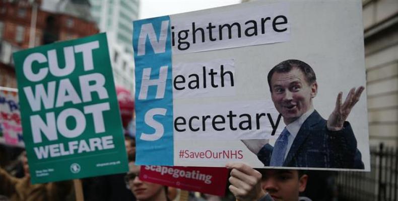 Protesters carry placards featuring Britain's Health and Social Care Secretary Jeremy Hunt during a march calling for an end to the &quot;crisis&quot; in the st